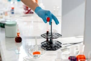 Technicien de laboratoire manipulant un tube à essai dans un portoir, au milieu de matériel d’analyse en laboratoire.
